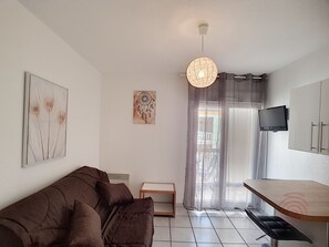 A modern living room with a brown sofa, a small wooden table, a TV mounted on the wall, and a ceiling light fixture.