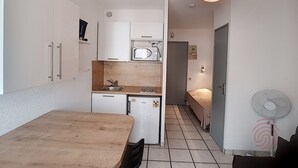 Una cocina compacta equipada con microondas, lavamanos y un refrigerador pequeño. Incluye una mesa de comedor con sillas, un ventilador de techo y una lámpara.