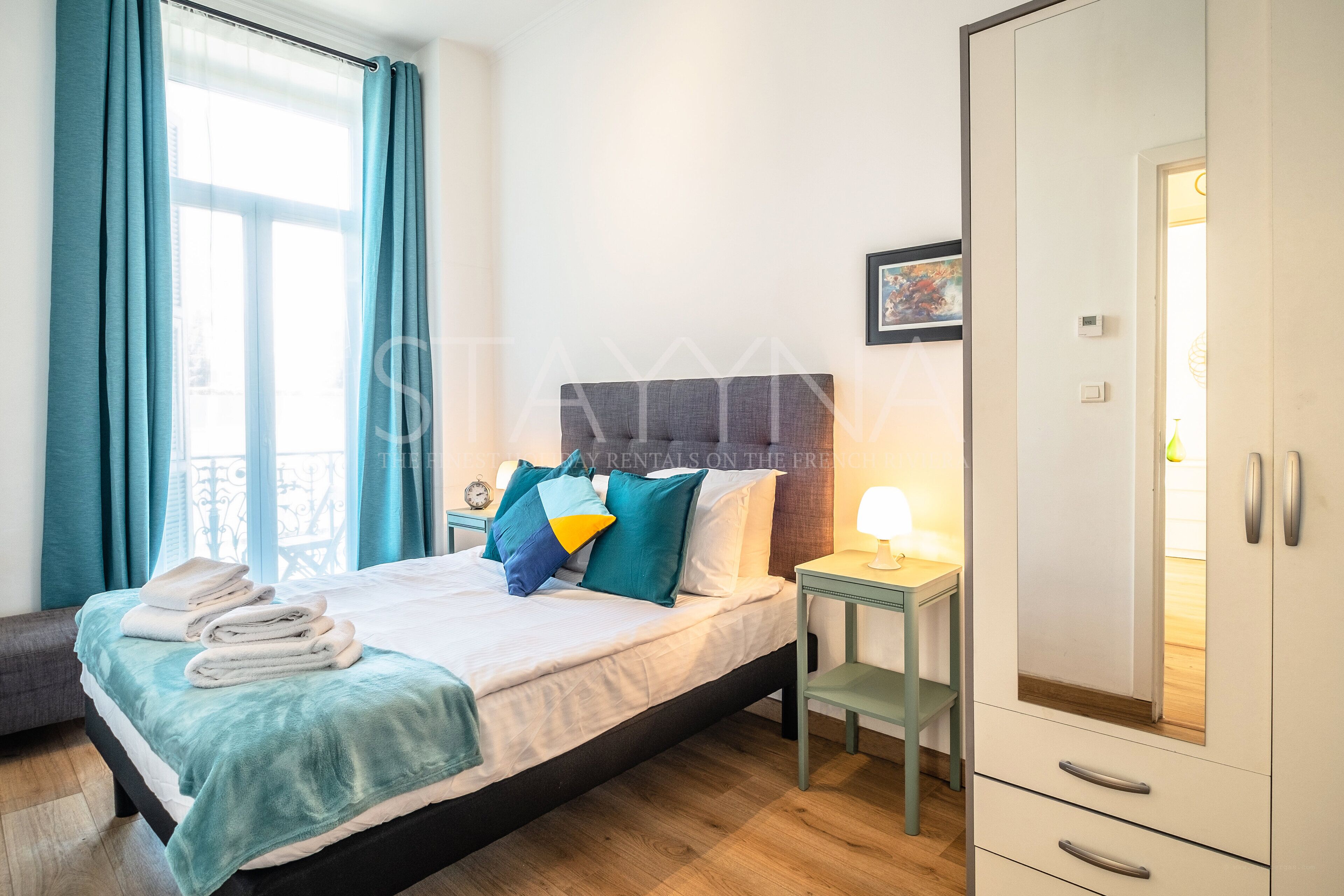Une chambre d’hôtel avec un lit, une table de chevet, une armoire et une fenêtre avec des rideaux.