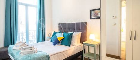 Une chambre d’hôtel avec un lit, une table de chevet, une armoire et une fenêtre avec des rideaux.