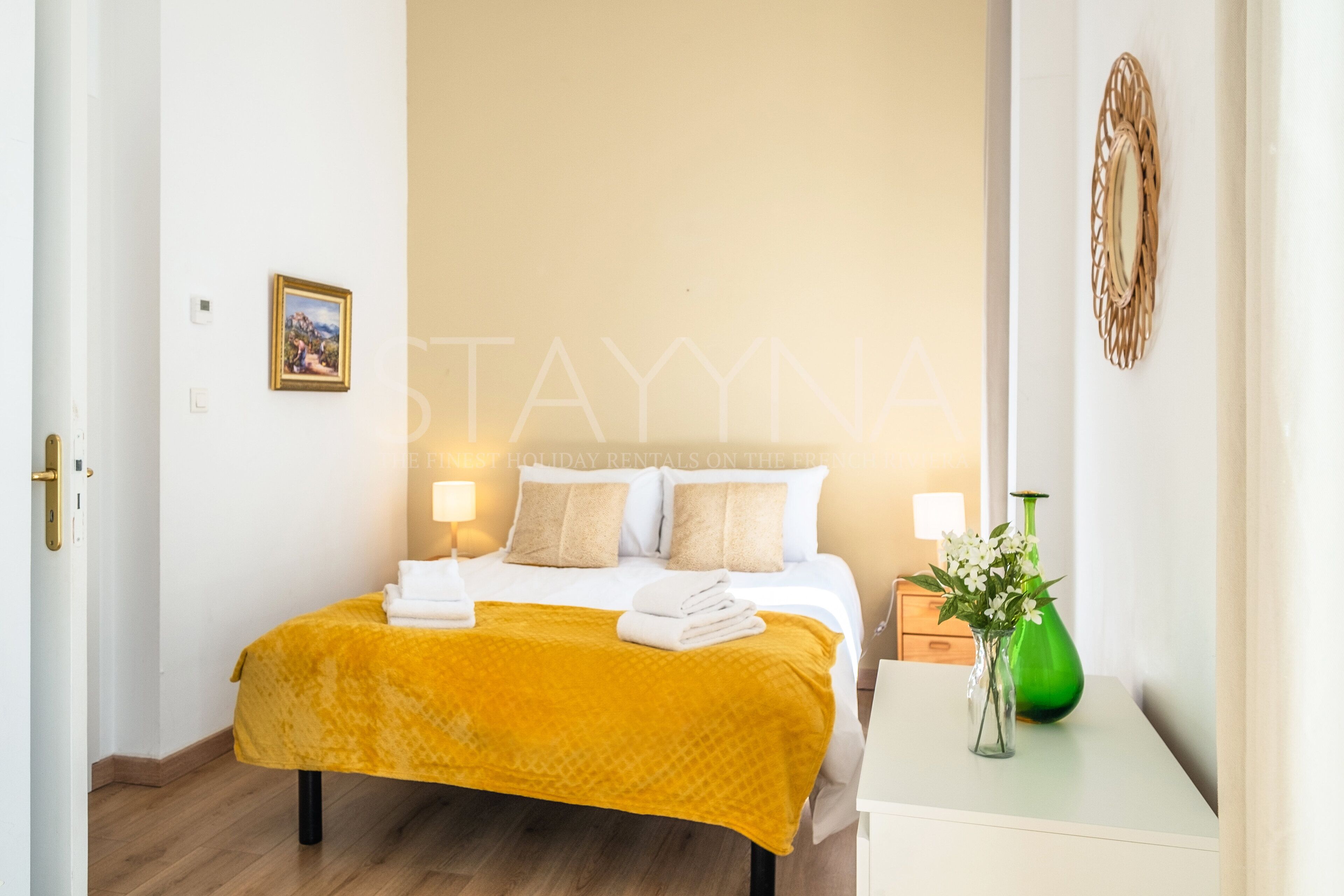 Ein Hotelzimmer mit einem Bett, einem Nachttisch mit Blumenvase und einem Wanddekor.
