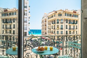 A balcony with a table set for breakfast, overlooking a coastal cityscape with historic buildings and a clear blue sea. - Californie 3 bedroom apartment VRBO (Nice)