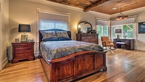 A bedroom with a wooden ceiling, a large bed with a patterned bedspread, a dresser, a chair, and a desk with a mirror. - Spacious & Updated 1920's HSNP Craftsmen Home (Hot Springs)