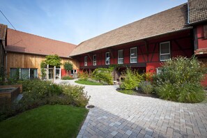 Ein Innenhof mit gepflastertem Weg, umgeben von einem roten Gebäude mit Ziegeldach und einer Holzkonstruktion auf der linken Seite.