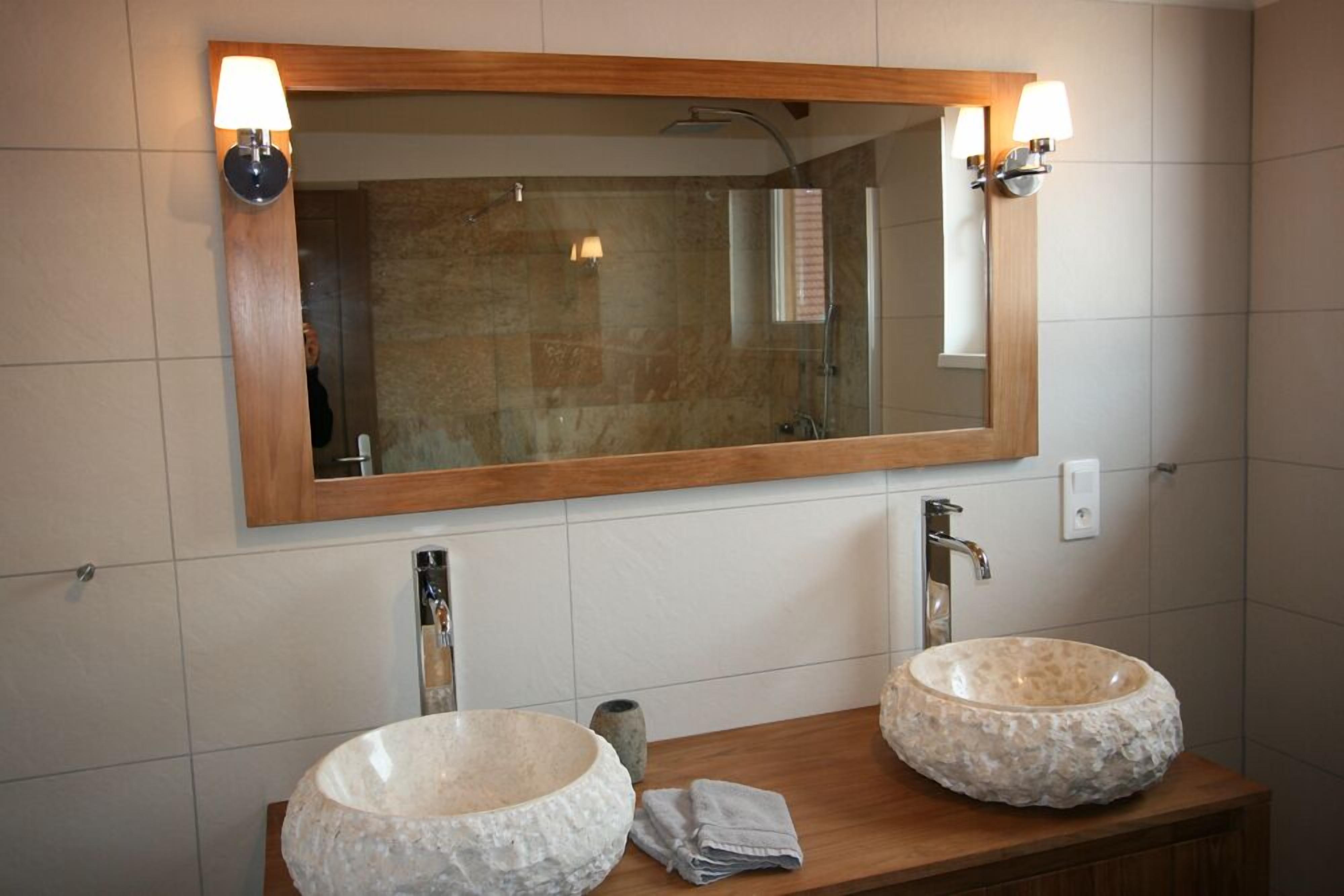 A bathroom with a wooden vanity, two stone sinks, and a large mirror with wall-mounted lights.