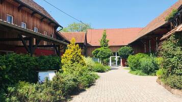 En traditionell byggnad i trä med ett rött tegeltak, en stenlagd gångväg och frodig grönska.