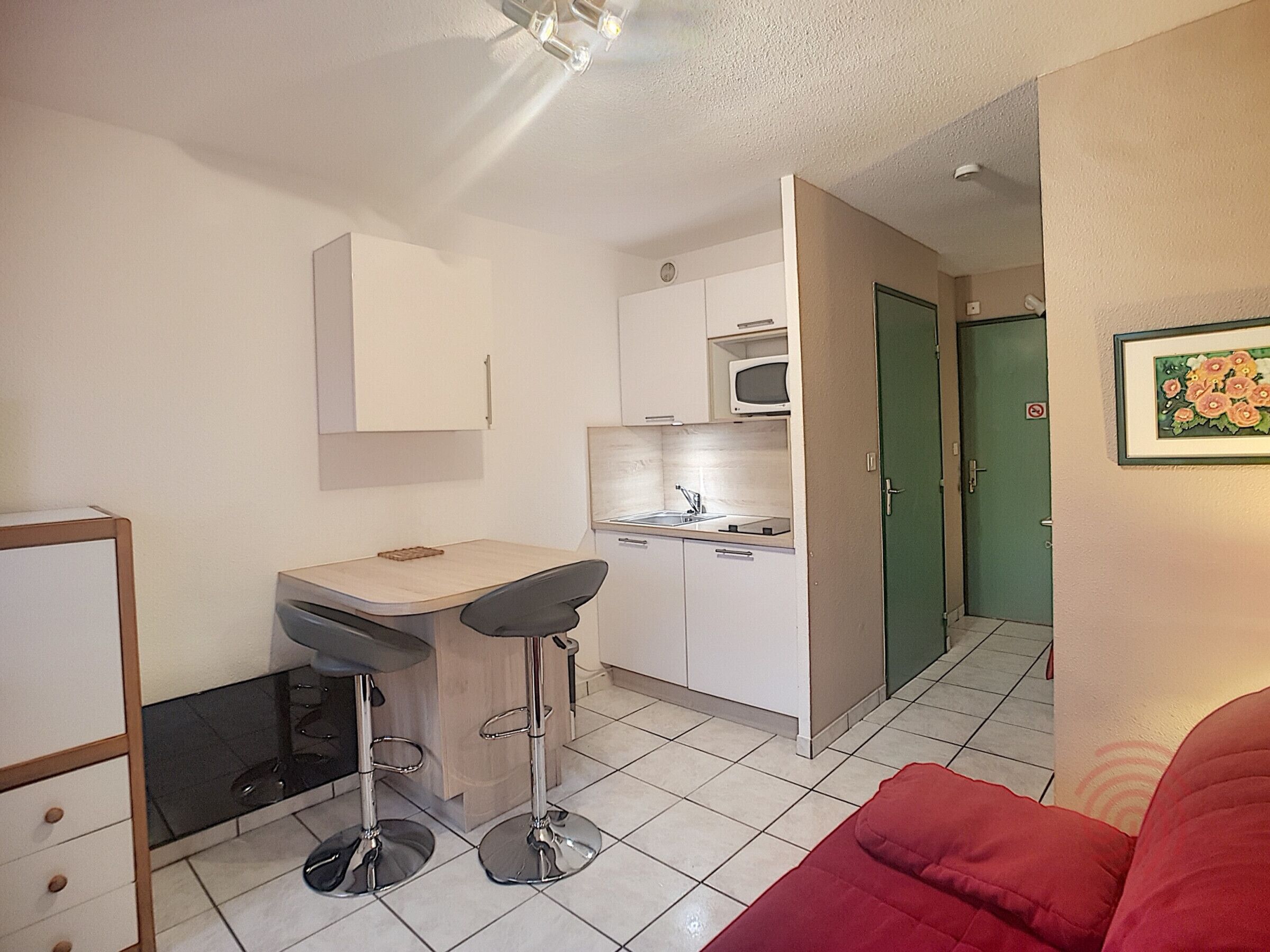 A compact kitchen with a microwave, a sink, and a small dining area with two stools.