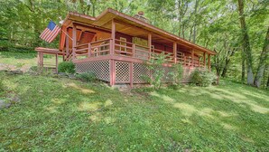A cabin with a porch, surrounded by trees and grass.