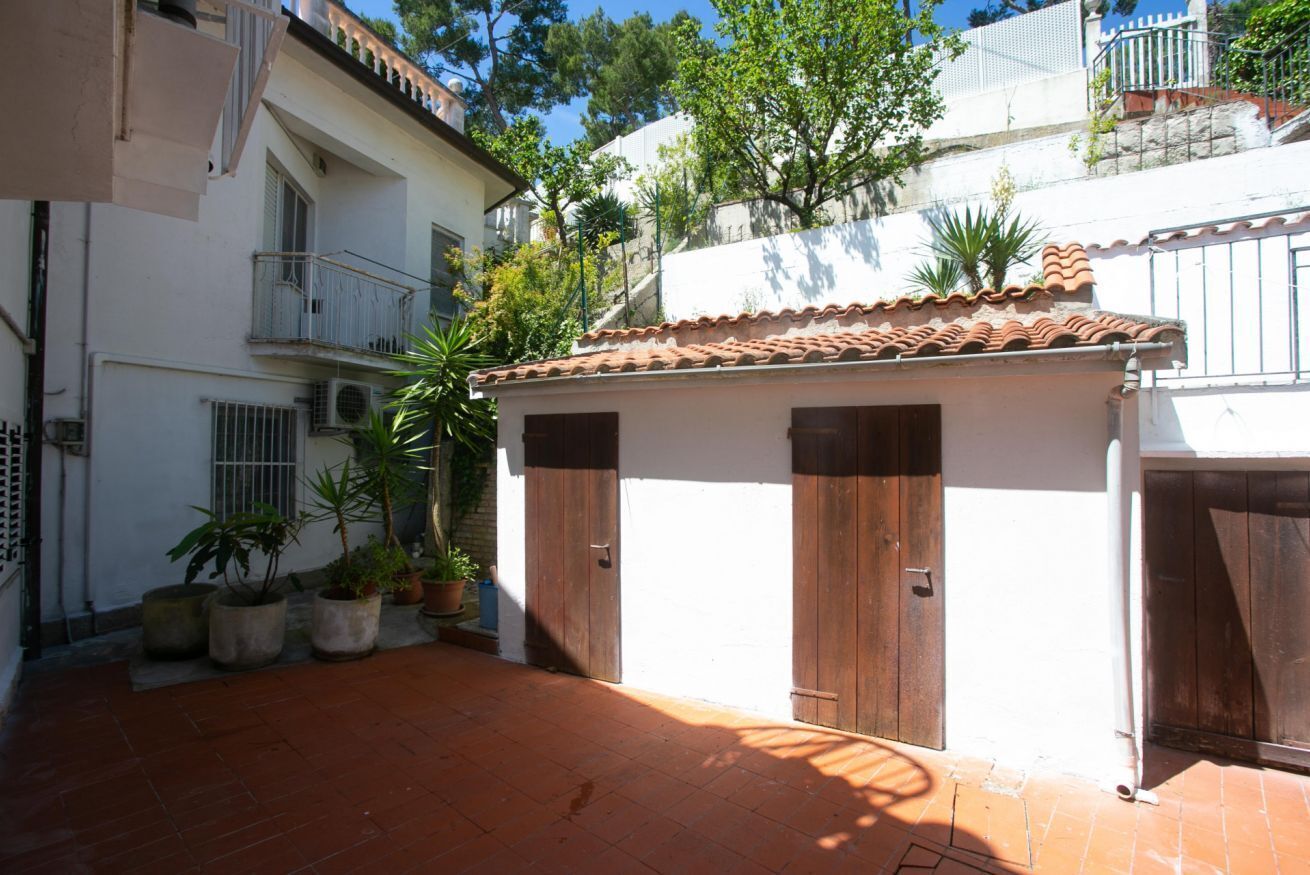 A courtyard with a tiled floor, potted plants, and a building with a tiled roof and wooden doors.