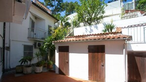 Une cour avec un sol carrelé, des plantes en pot et un bâtiment doté d’un toit en tuiles et de portes en bois.