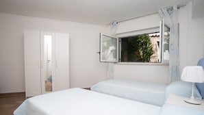 Une chambre avec deux lits, une fenêtre avec des rideaux, une table de chevet avec une lampe et une armoire.