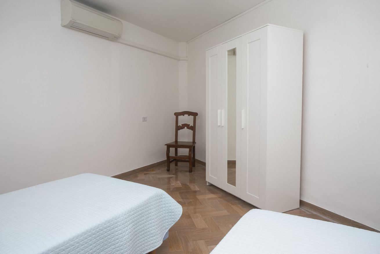 A small, clean room with two beds, a wooden chair, and a white wardrobe.