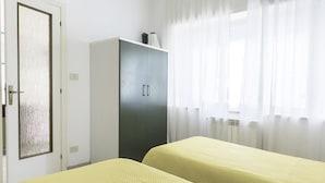 A room with two beds, a wardrobe, a door with a frosted glass panel, and a window with sheer curtains. - N050 - Numana, three-room apartment in the center with porch and parking space (Numana)
