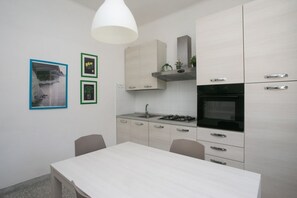 Une cuisine moderne avec des meubles blancs, une cuisinière à gaz et un four à micro-ondes. On y trouve une table à manger avec des chaises.