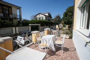Une terrasse extérieure avec des tables et des chaises, une voiture et un bâtiment en arrière-plan.