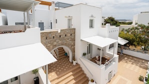 A modern white building with a stone wall, a staircase, and a small outdoor seating area. - Erato Inn (Naxos)