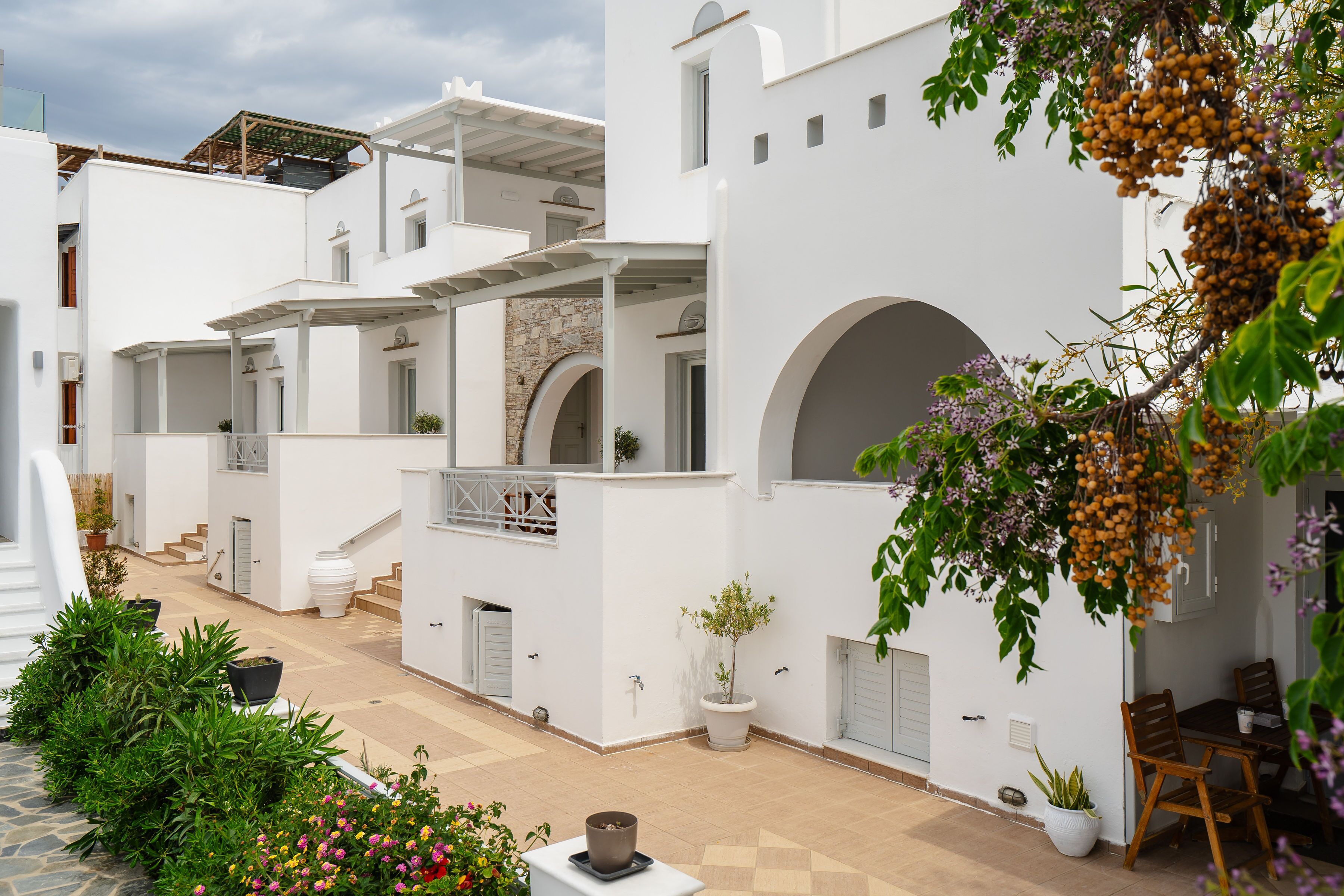 A white building with a covered outdoor area, potted plants, and a table with chairs.