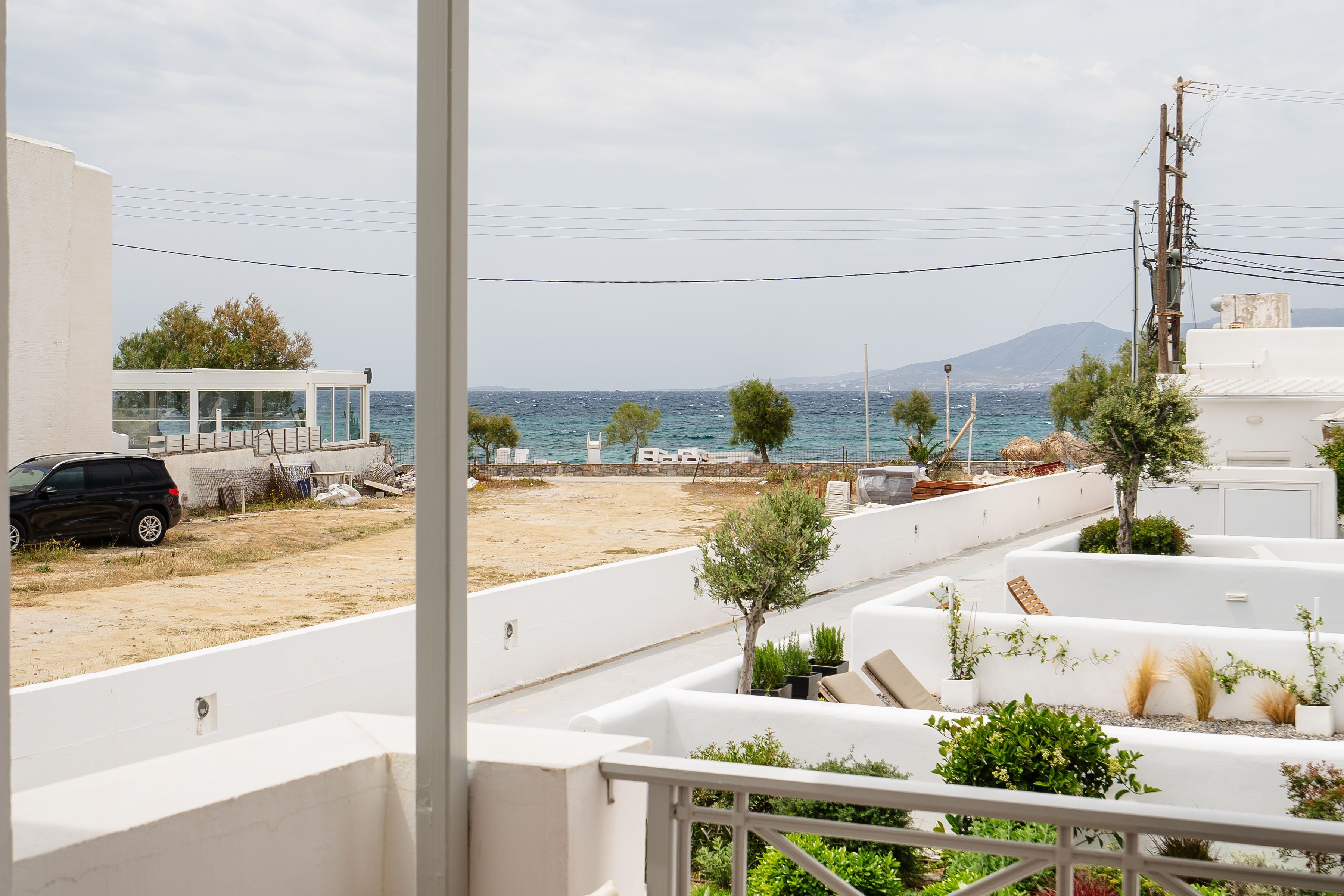 A coastal property with a terrace overlooking the sea, a parked car, and a white building with a glass structure.