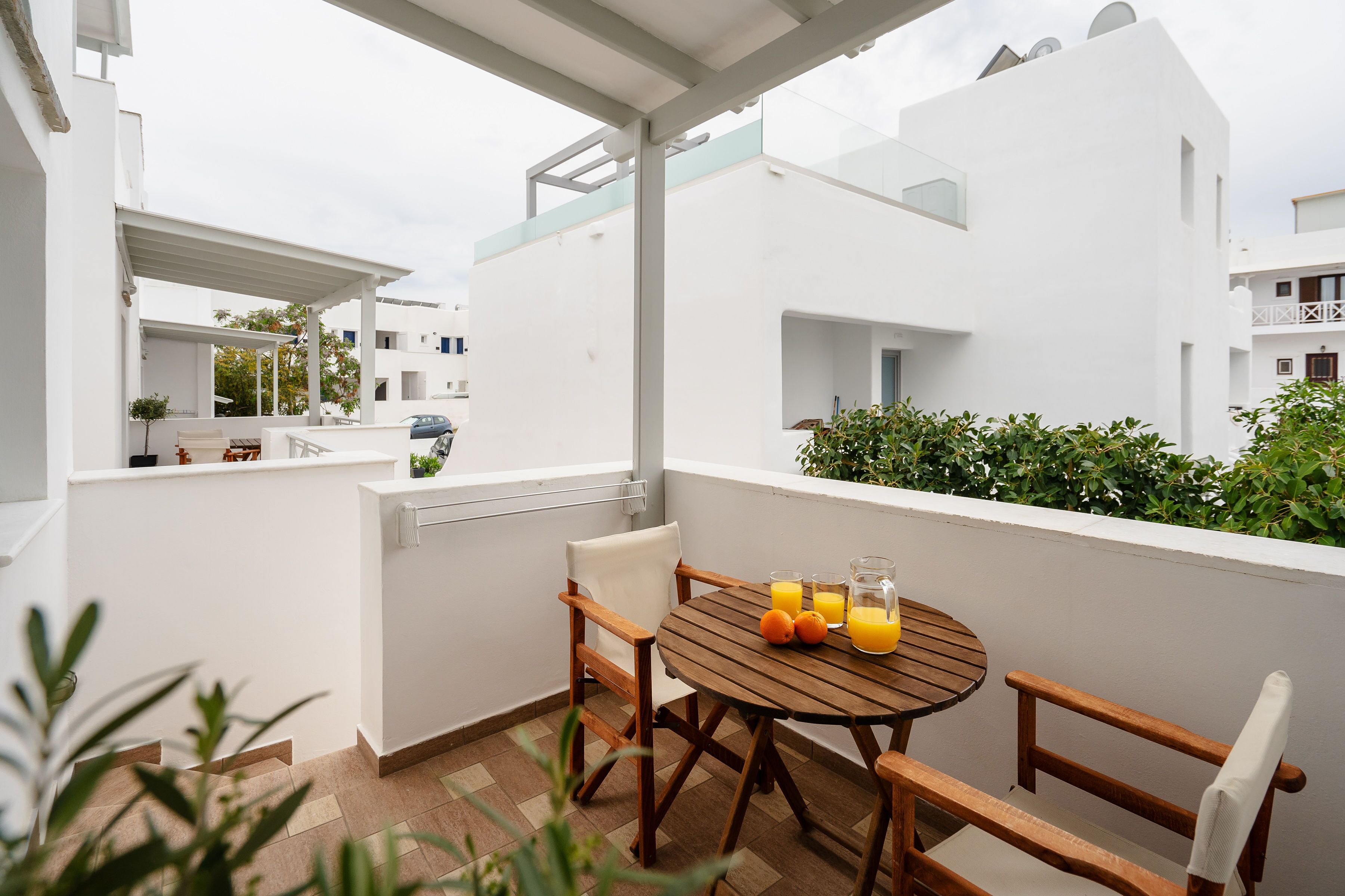 Uma varanda com mesa e cadeiras de madeira, um pequeno vaso de planta e um copo de sumo de laranja.