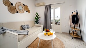 A modern living room with a sofa, a round coffee table with drinks, a plant, and a clothing rack. - Erato Inn (Naxos)