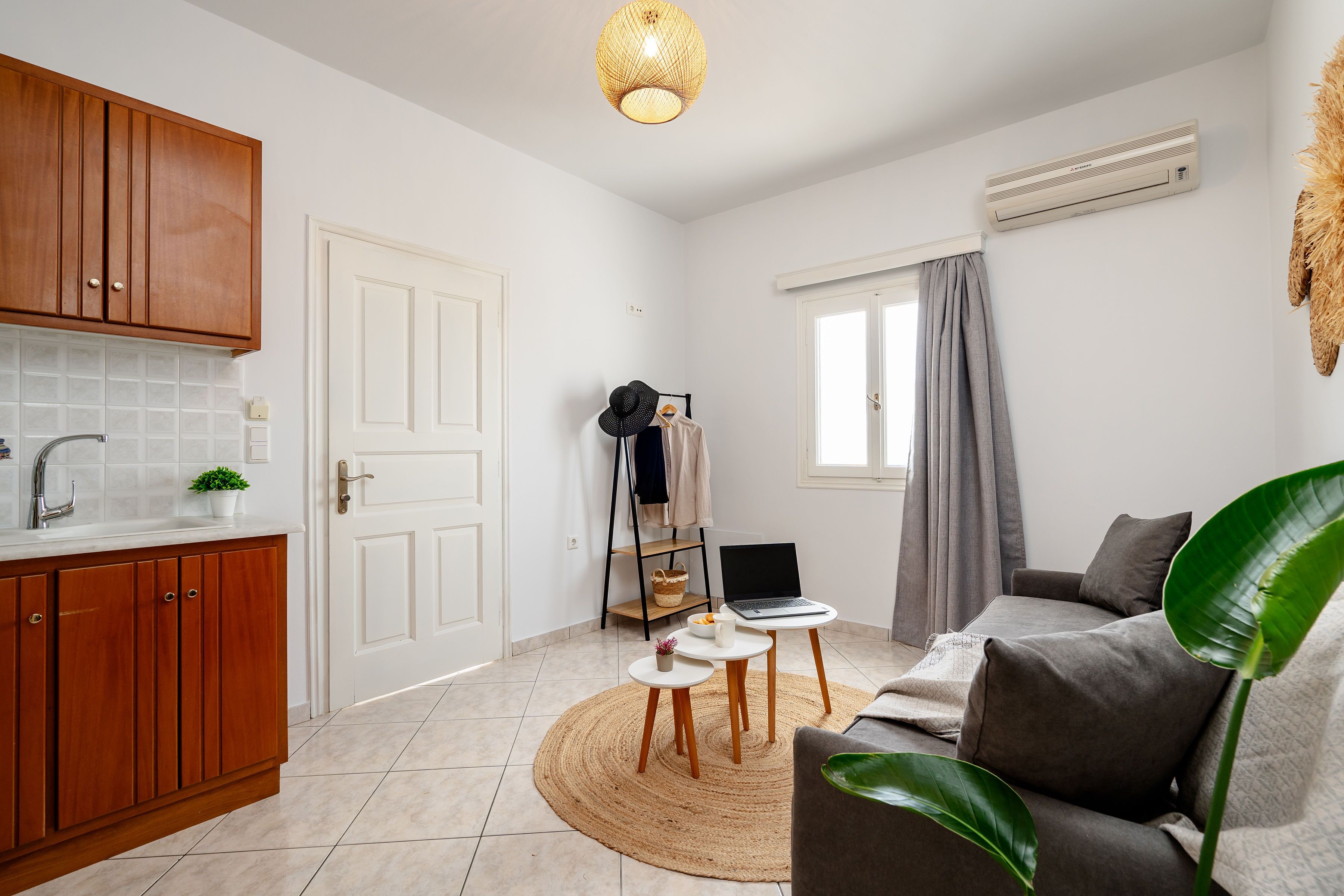 A compact living space with a kitchenette, a sofa, a dining table, and a laptop on a small table.