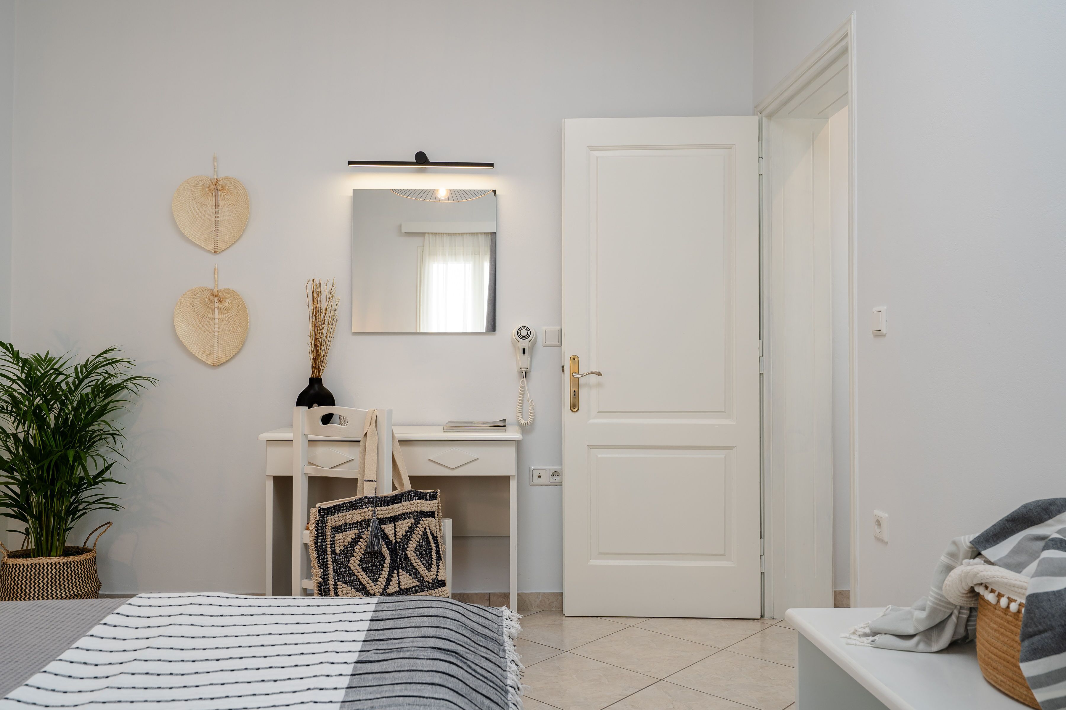 Une chambre à coucher comprenant un lit, une table de chevet, un bureau avec une chaise, un miroir et une porte.