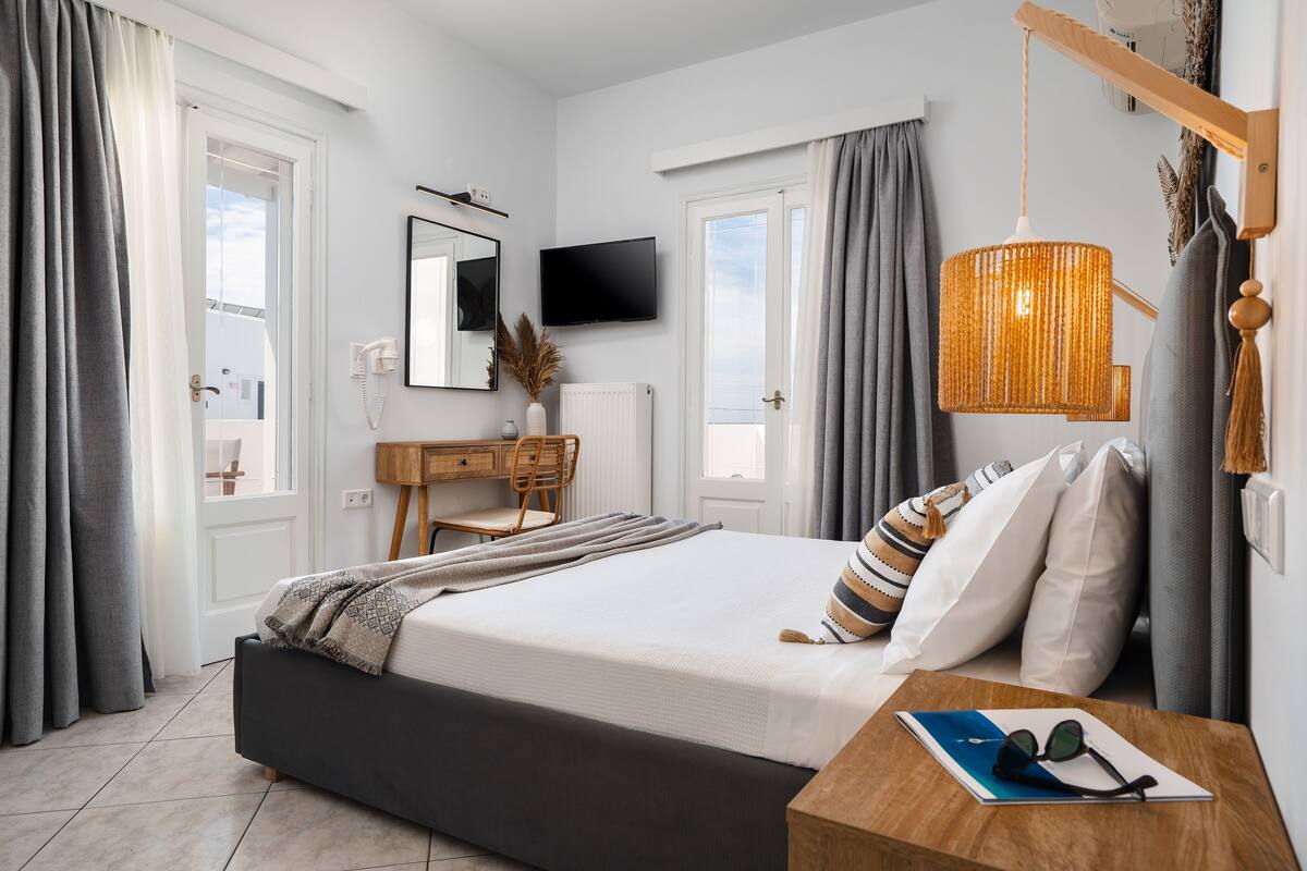 A bedroom with a bed, a desk, a chair, a TV, and a hanging light fixture.