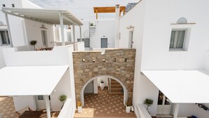 A courtyard with a stone archway, white buildings, and a wooden staircase. - Erato Inn (Naxos)