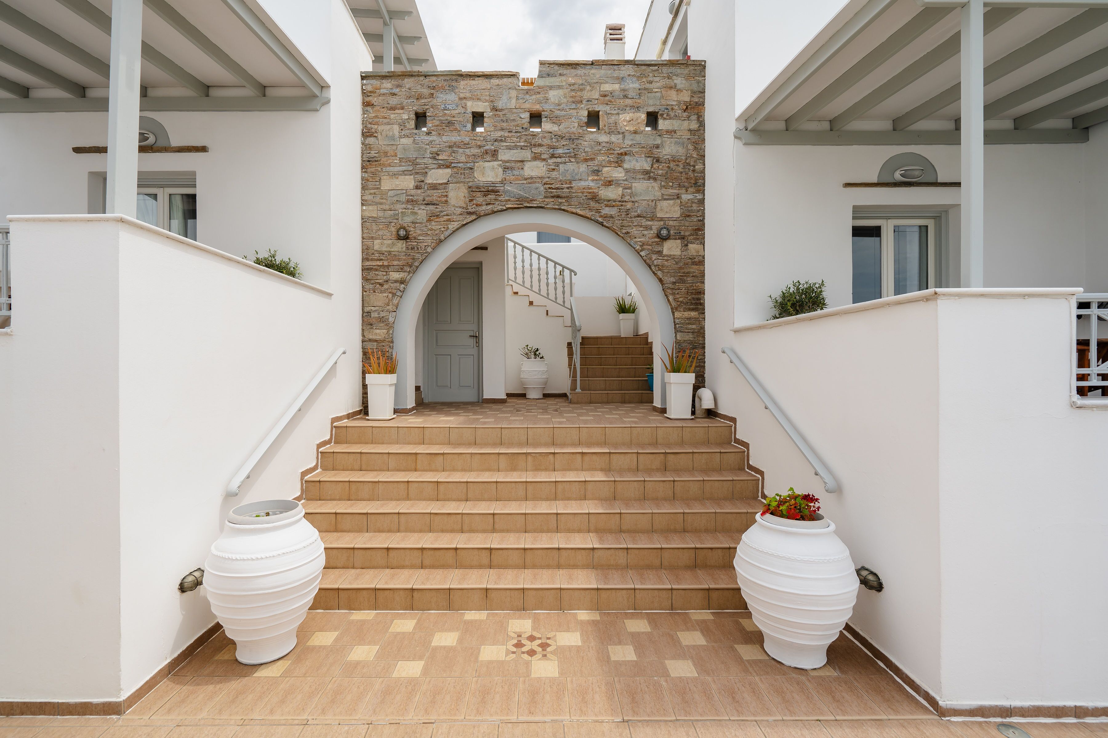 A staircase leading to a door with a stone wall archway, flanked by two large white planters.