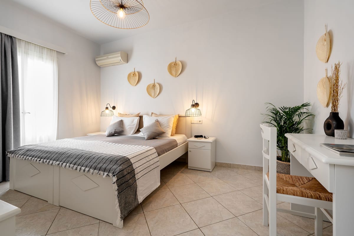 A modern bedroom with a bed, bedside tables, a desk, and a potted plant.
