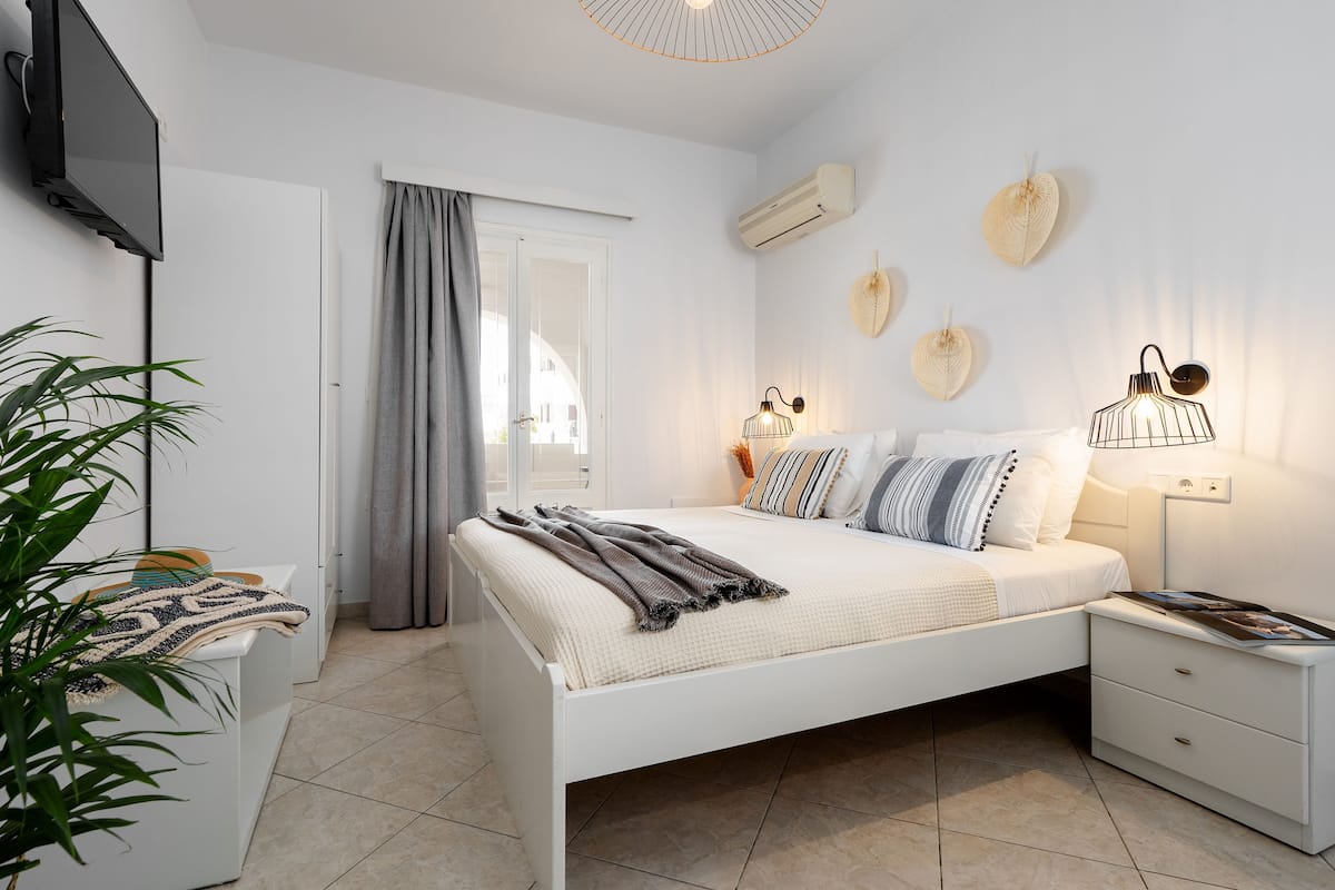 A bedroom with a bed, bedside tables, a TV, and a plant.