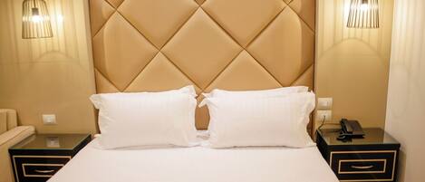 A hotel room with a tufted headboard, two bedside tables with lamps, a bed with white linens, and a telephone on one of the tables.