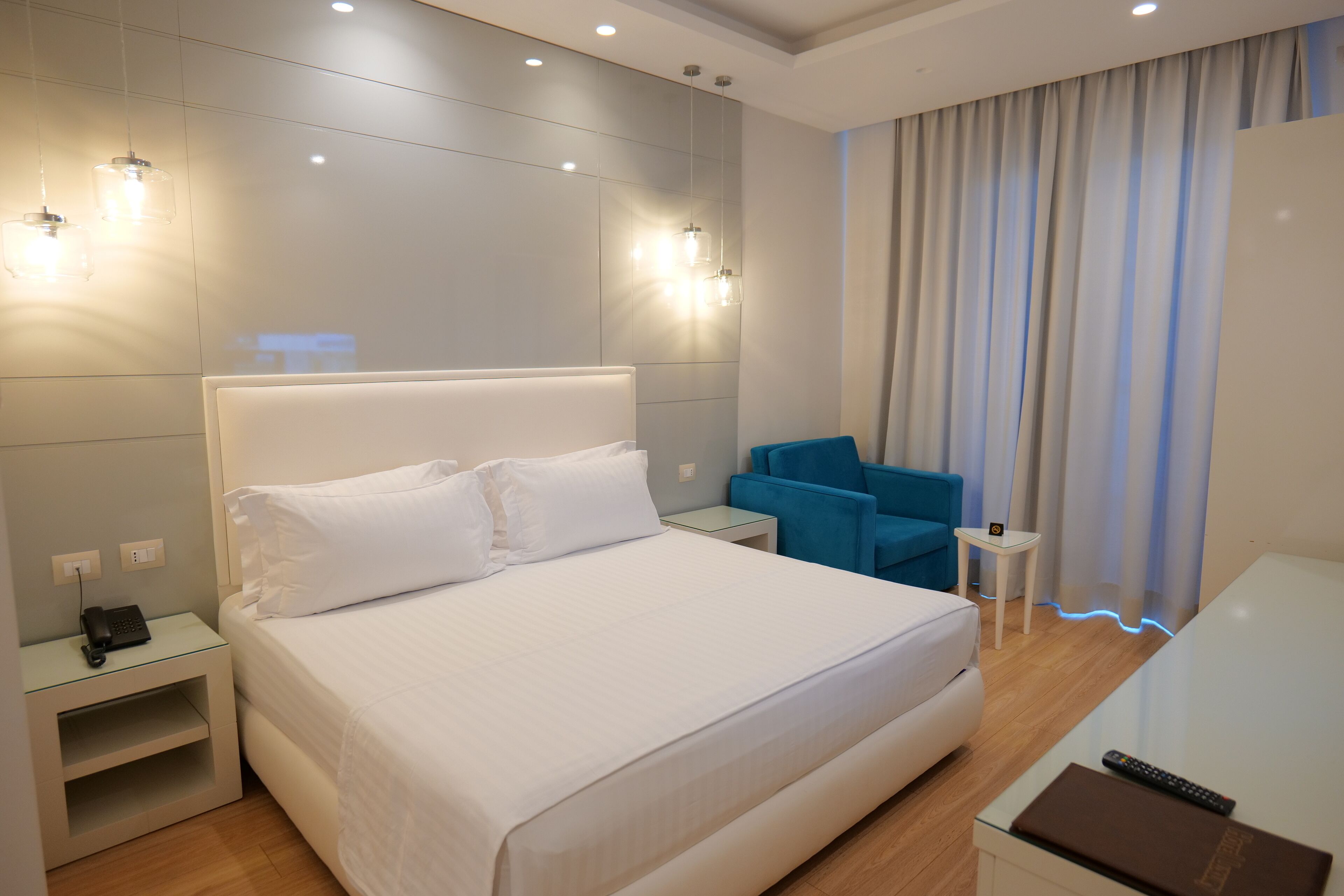 Une chambre d’hôtel moderne avec un grand lit, des tables de chevet, un bureau, une chaise et une vue sur la ville, visible à travers les rideaux.