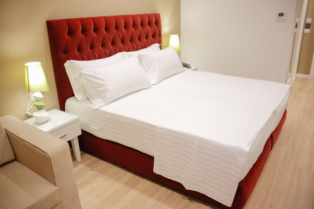 Una cama bien hecha con sábanas blancas, un cabecero tapizado rojo y dos lámparas de noche.