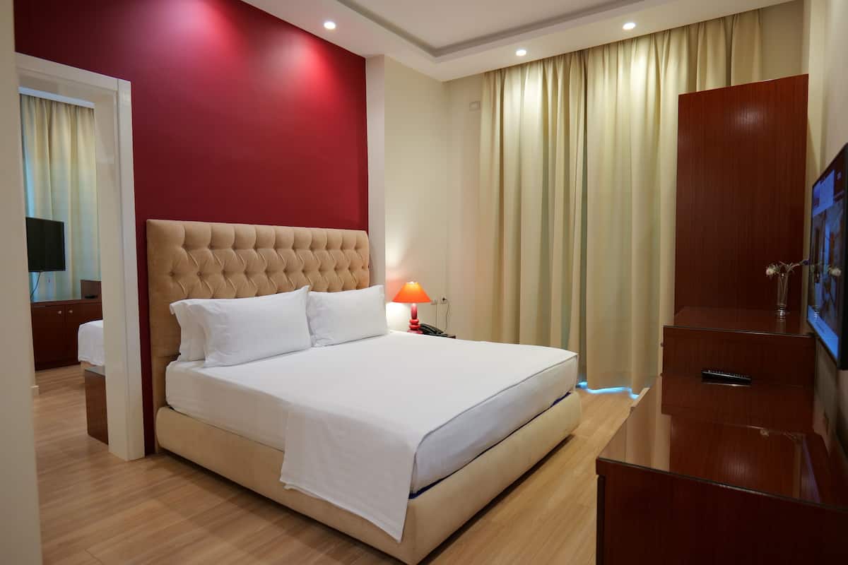 A hotel room with a large bed, a wooden dresser, a TV, and a lamp.