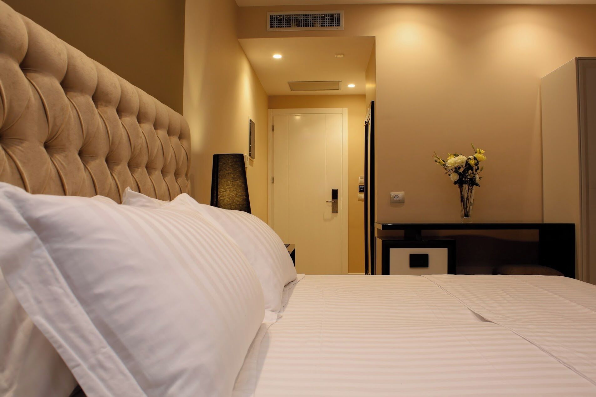 A hotel room with a large bed, a bedside table, a mirror, and a door leading to another room.