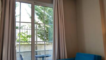 A room with a blue sofa, a small white table, and a glass door leading to an outdoor area with chairs.