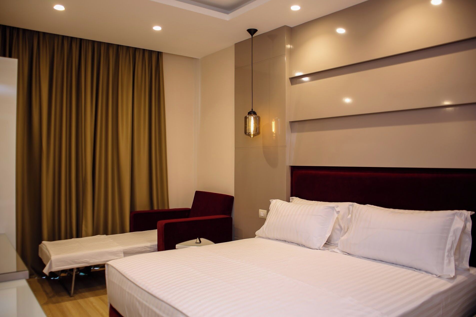 A hotel room with a large bed, a chair, a bedside table, and a curtain.