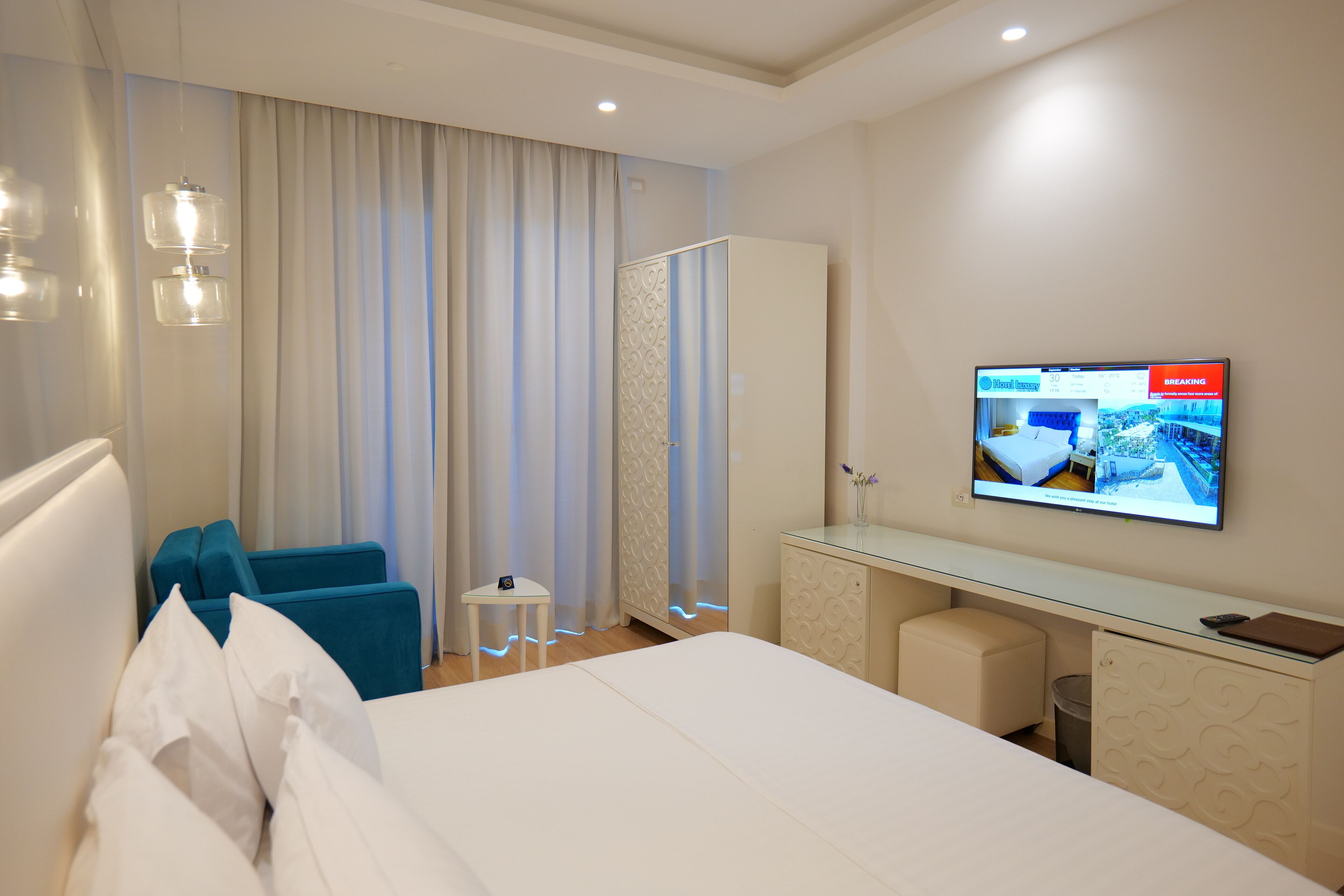 Una habitación de hotel con cama, escritorio, televisor, armario y una mesita.