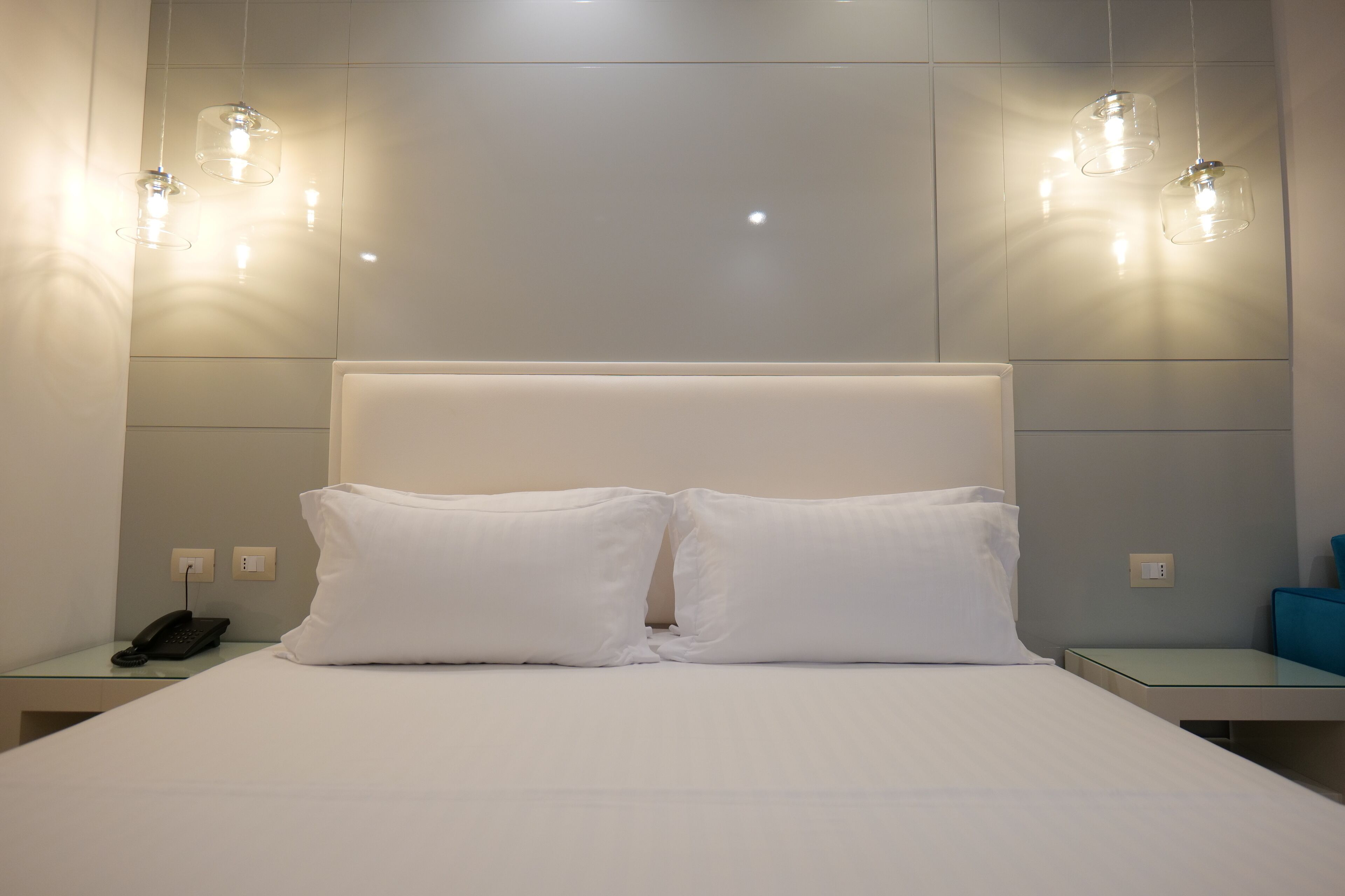 Een hotelkamer met een groot bed, twee nachtkastjes, een telefoon en hangende lampen.