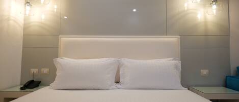 A hotel room with a large bed, two bedside tables, a telephone, and pendant lights.