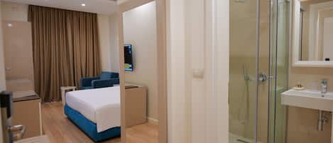 Una habitación de hotel moderna con cama, escritorio, televisión, zona de ducha y baño con lavamanos.