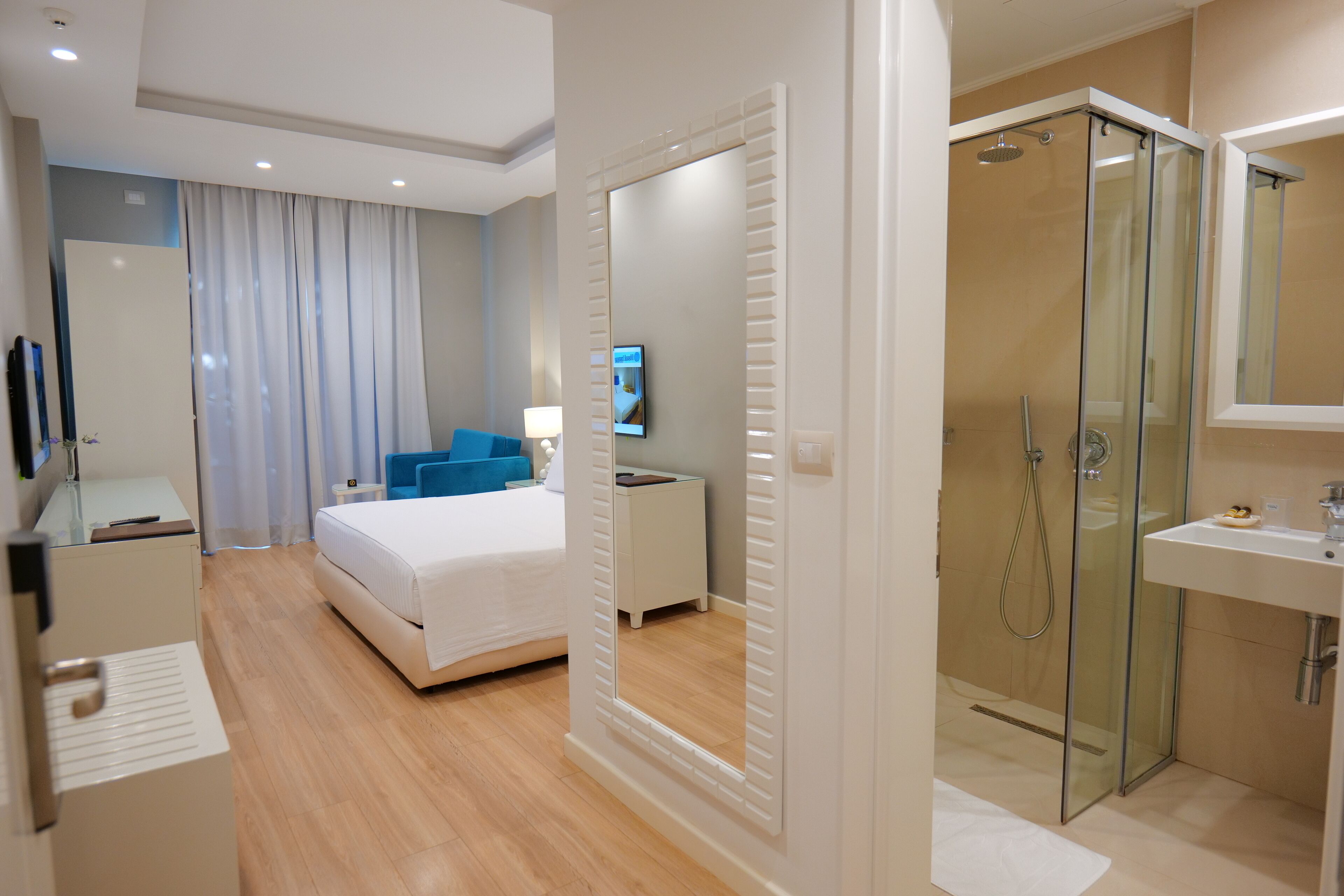 A modern hotel room with a bed, a desk, a TV, a shower, and a bathroom.