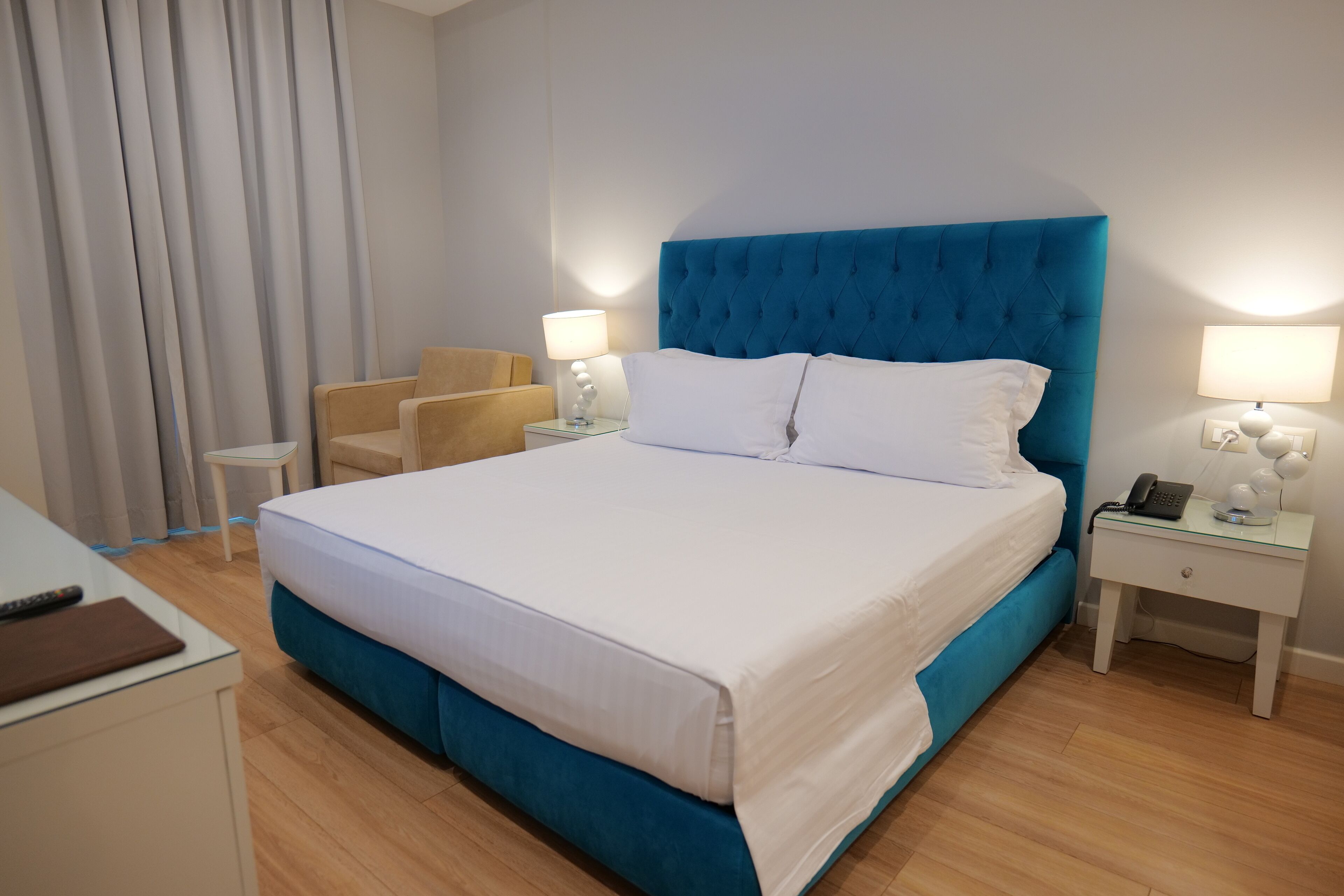 A hotel room with a large bed, two bedside tables, a chair, and a desk with a lamp.