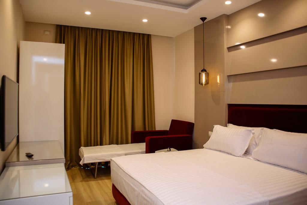 Una habitación de hotel con una cama grande, una cama más pequeña, un escritorio con una silla, un televisor y una ventana con cortinas.