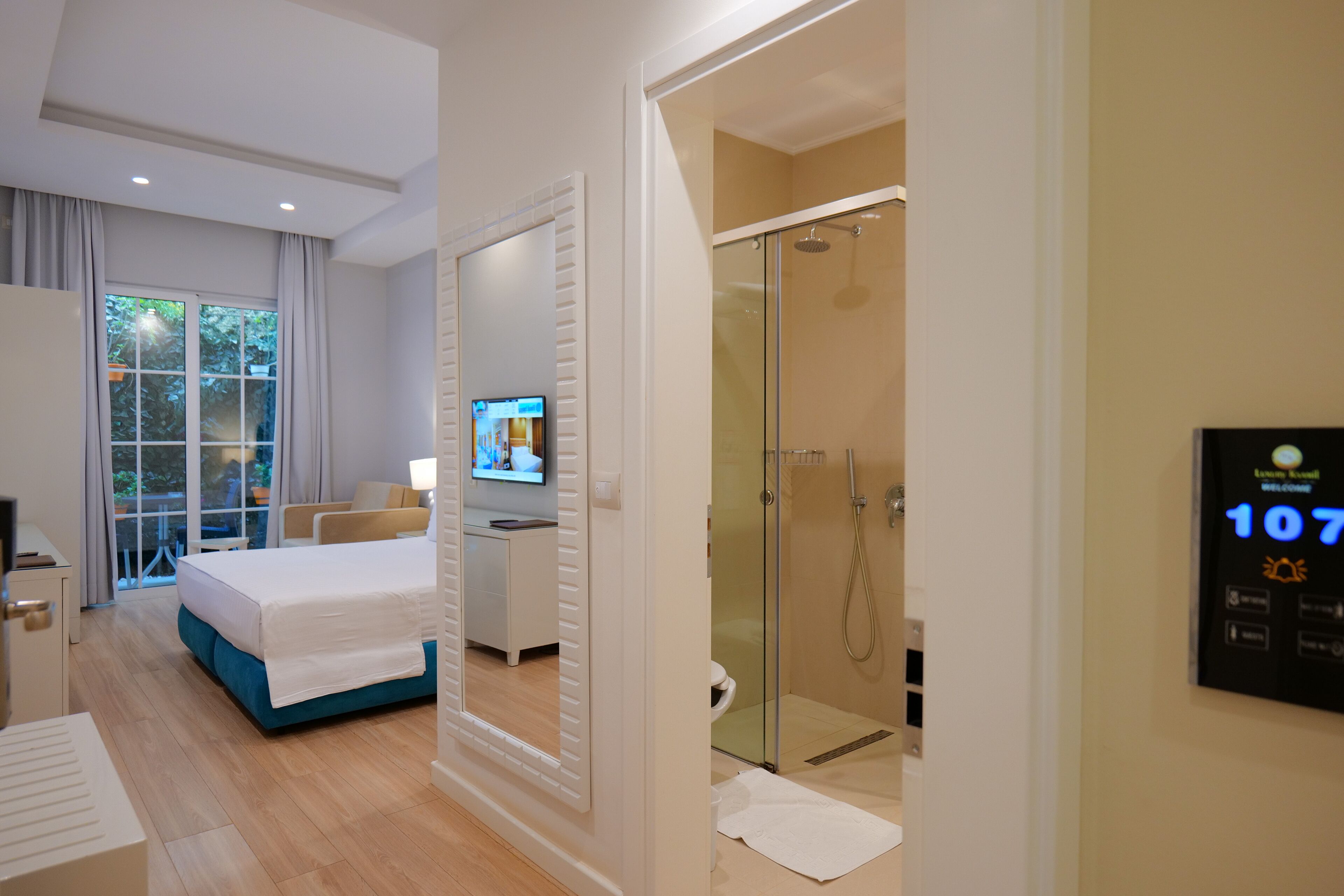 Habitación de hotel moderna con cama, televisor, ducha y pantalla digital de bienvenida.
