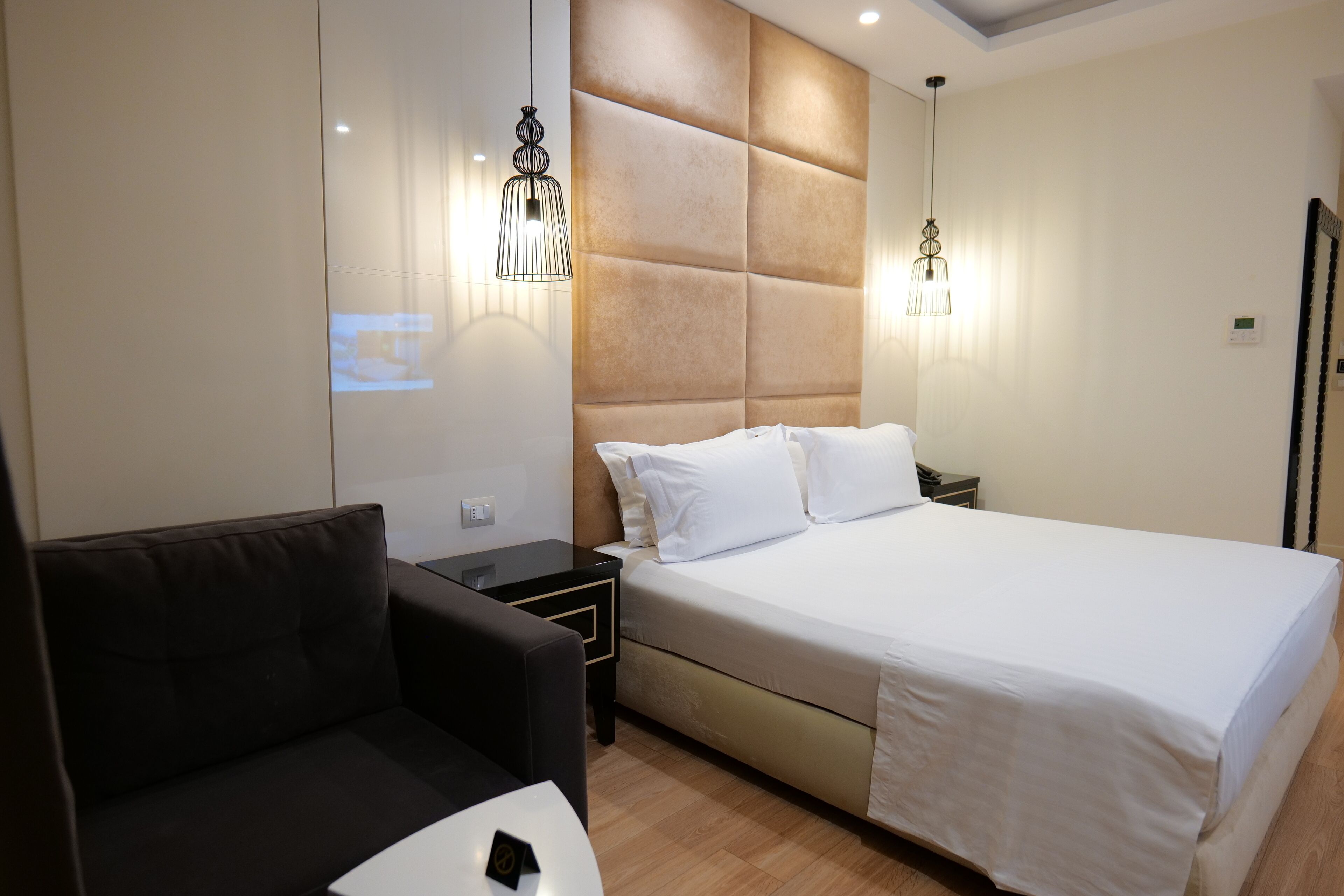 A modern hotel room with a large bed, a small sofa, and two bedside tables.