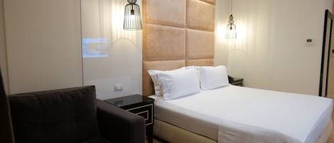 A modern hotel room with a large bed, a small sofa, and two bedside tables.