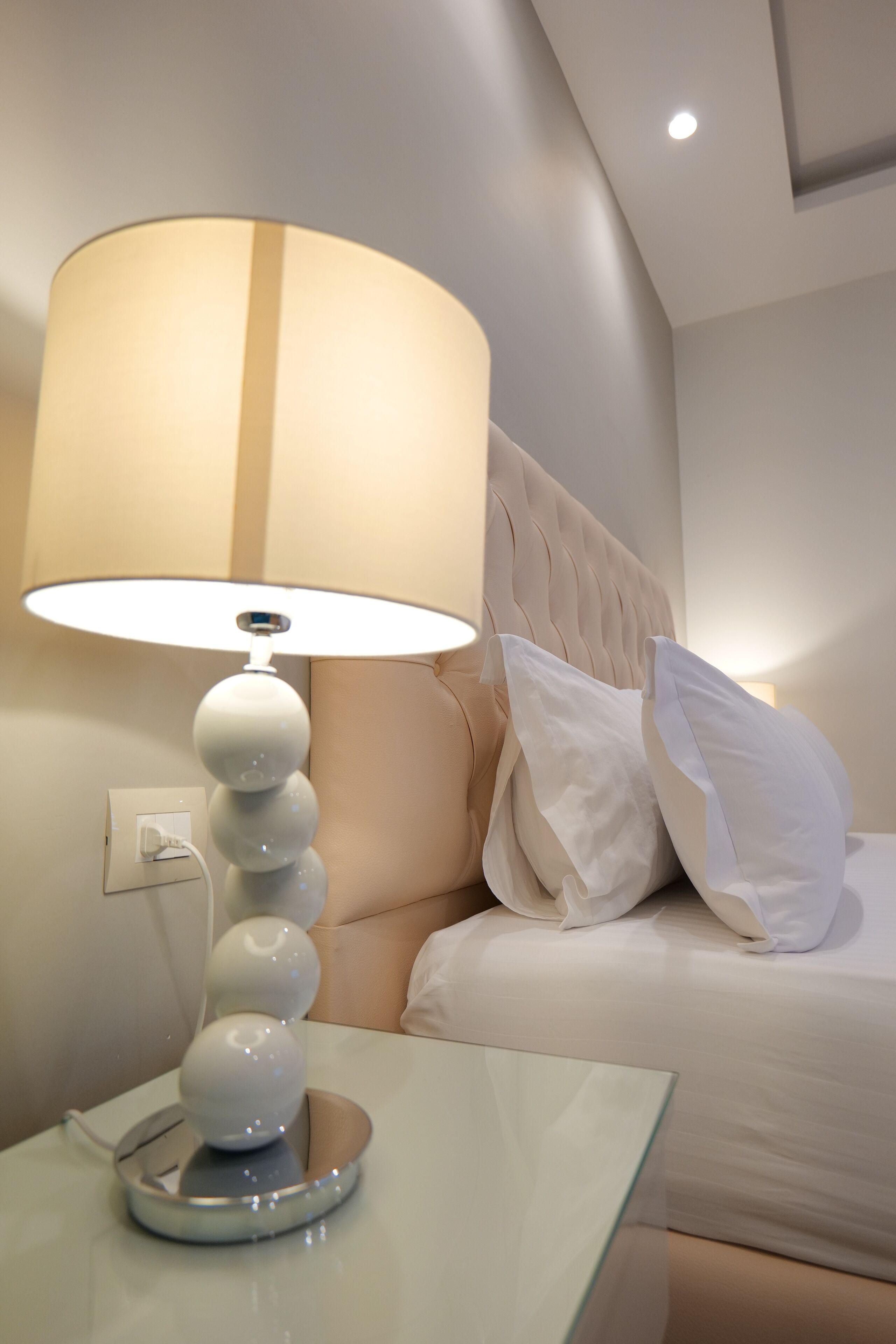 A modern hotel room with a bedside table, a lamp, a bed with white bedding, and a wall socket.