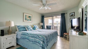 A bedroom with a bed, nightstand, lamp, ceiling fan, and a view of the outside. - CRC 2204 - Second Floor Ocean, Pool View Condo (St Augustine)